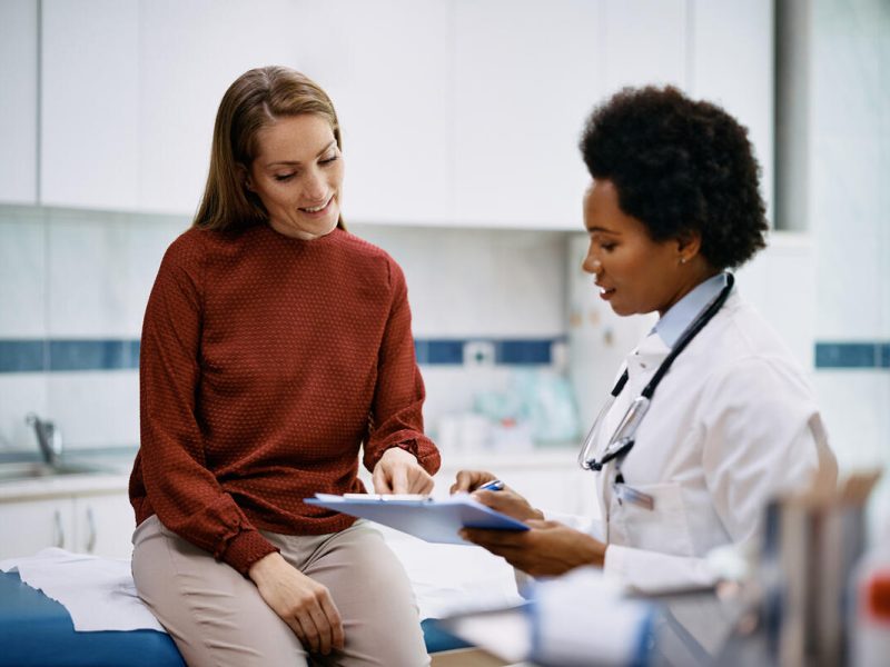 African American doctor and her female patient analyzing medical report after examination in the hospital. Focus is on female patient.